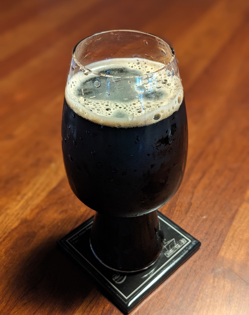 dark stout with tan head in tall, slightly bulged-out craft beer glass, sitting on table